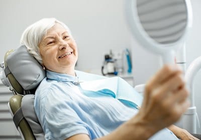 older woman admiring her smile in mirror with All on 4 dental implants in North Dallas