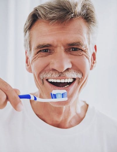 older man with moustache brushing his teeth 