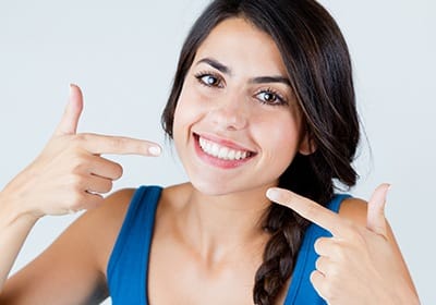 Woman pointing to her smile after cosmetic dentistry in North Dallas