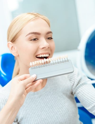 Dentist holding tooth color chart next to smiling patient