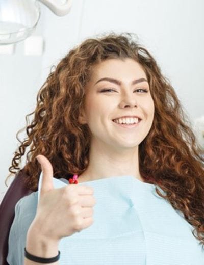 young woman smiling and giving thumbs up in dental chair