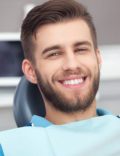 A young man with a beard smiling while seated in the dental chair