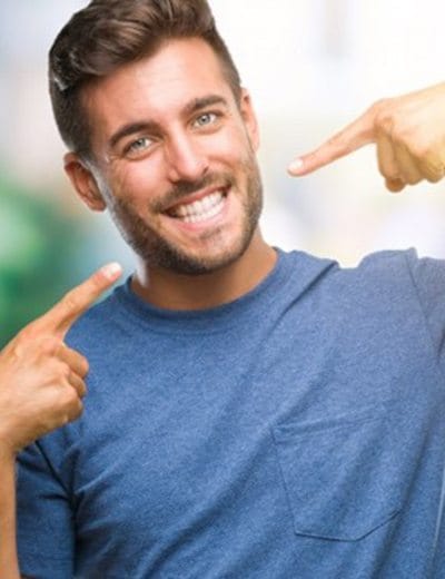 young man pointing to his smile after seeing his cosmetic dentist in North Dallas