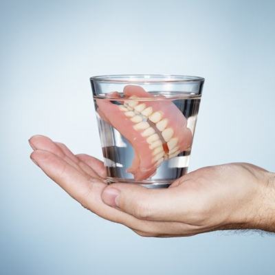 hand holding dentures in glass of water