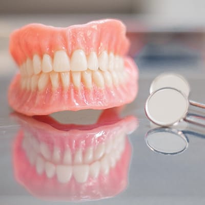 A set of dentures sitting on a table with a dental mirror lying next to them