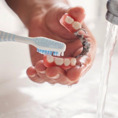 Hands brushing partial dentures with running water