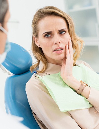 Woman holding her cheek in pain while visiting emergency dentist in North Dallas