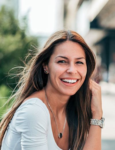 Woman with dental implants sitting outside and smiling