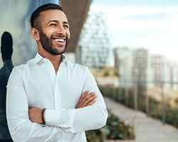 Man with dental implants smiling outside with his arms folded