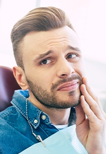 man holding jaw in pain in dental chair