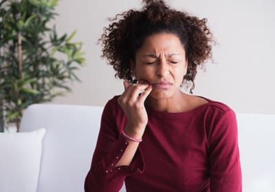 Woman holding her cheek in pain and needing gum disease treatment in North Dallas