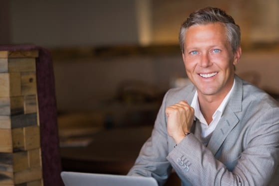 Smiling older man in suit sitting at desk with laptop