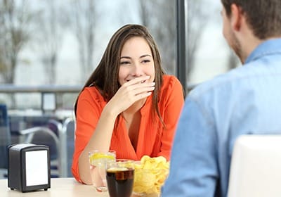 Woman covering her teeth while smiling at lunch