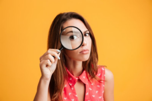 Woman looking through a magnifying glass on yellow background
