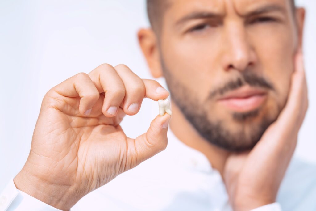Man holding extracted tooth with one hand and touching sore jaw with the other