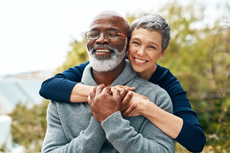 Older patient with dental implants smiling with partner 